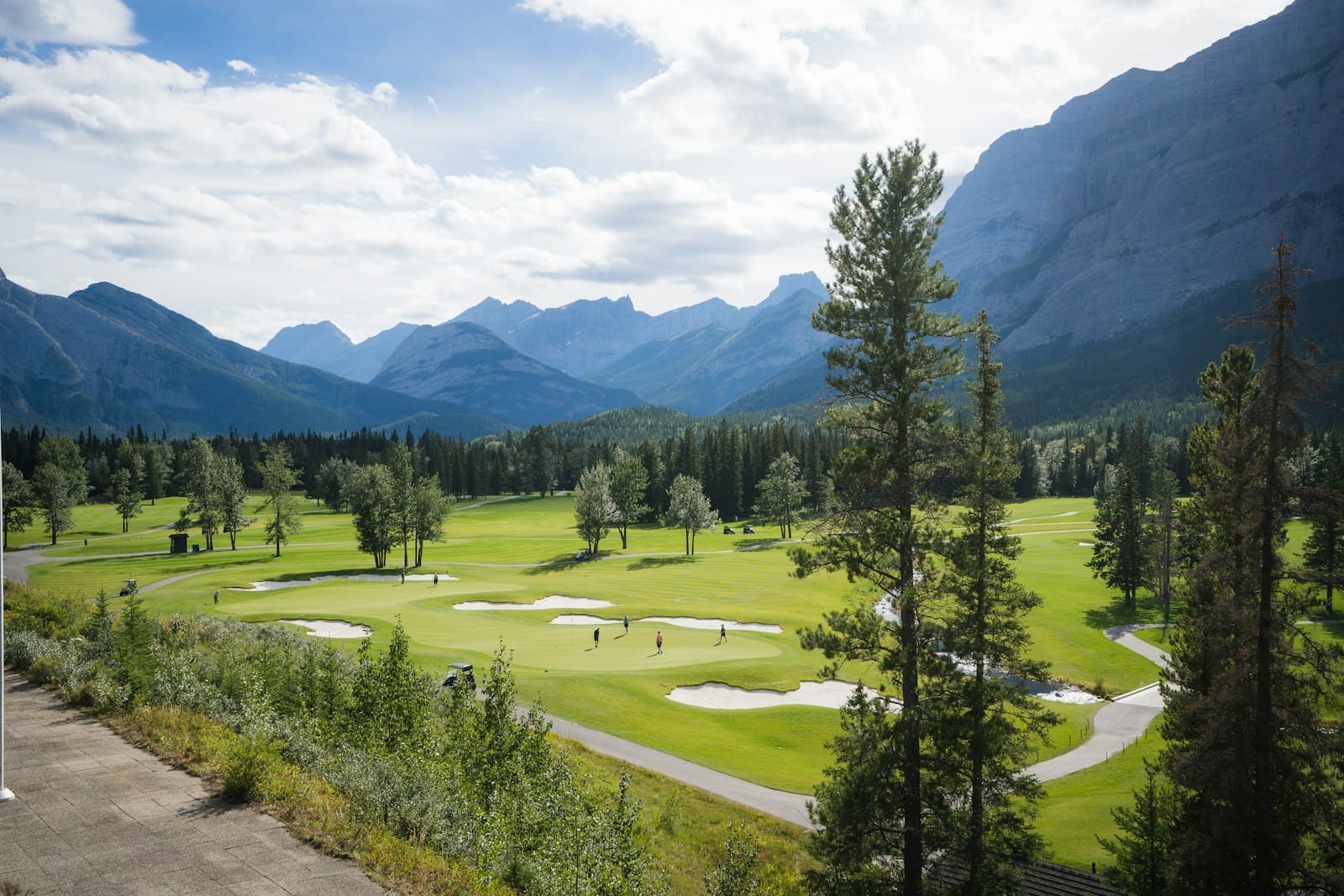 Green mountain golf course with sand bunkers framed by alpine peaks