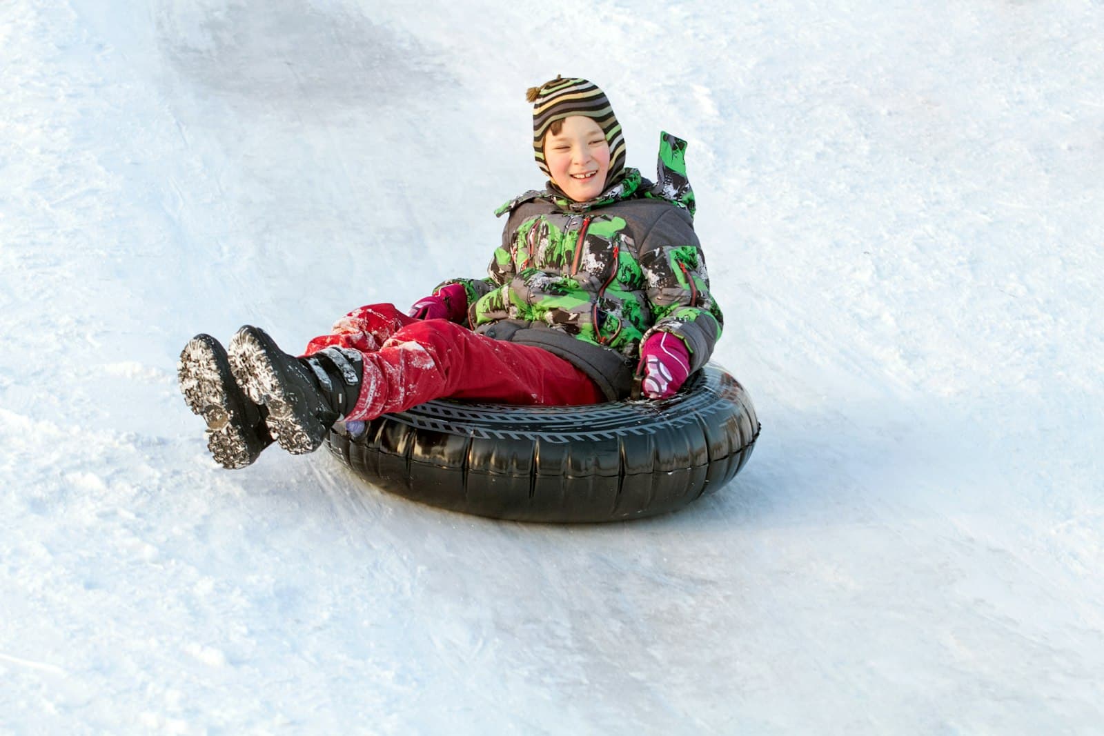 Smiling child riding a snow tube down a snowy slope