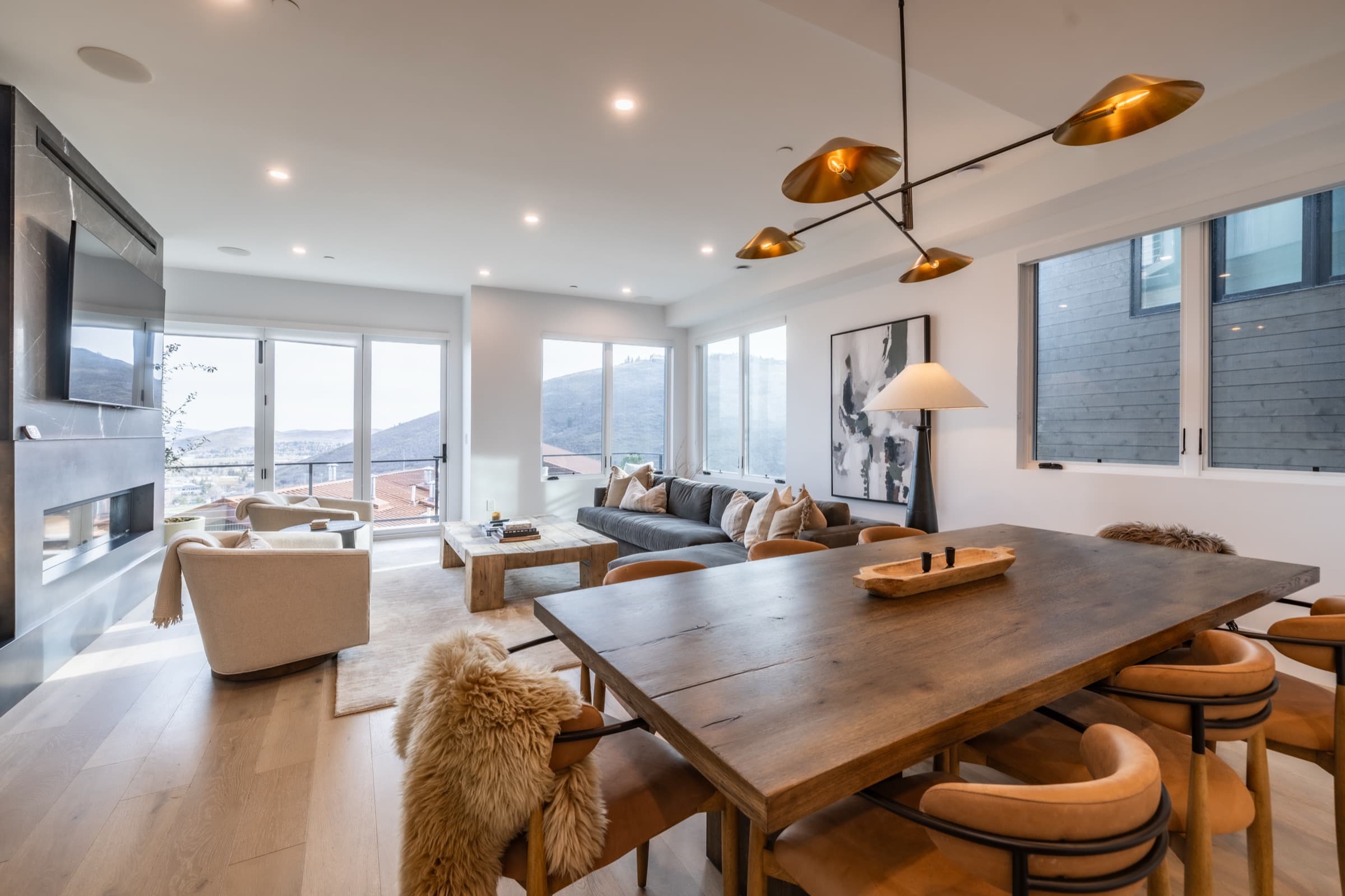 Open dining and living room with a long wood table, brass pendants, and mountain views