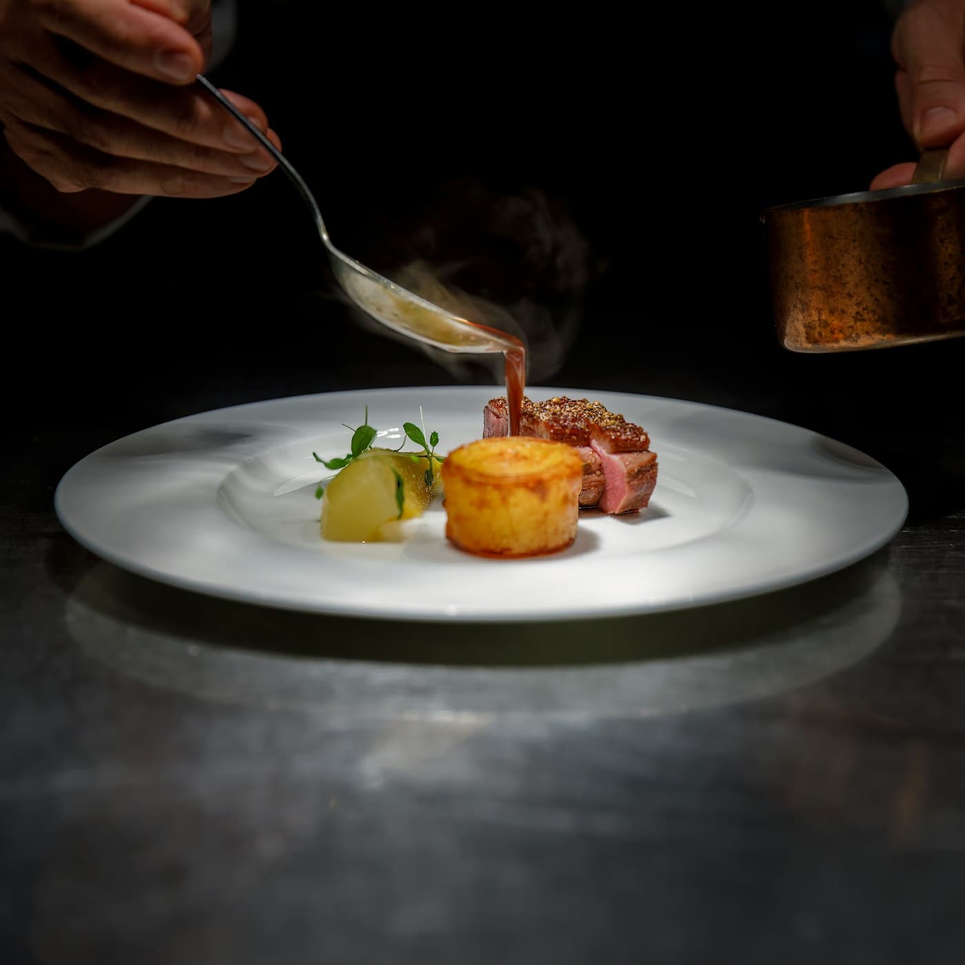 Private chef finishing a plated course in a restaurant kitchen