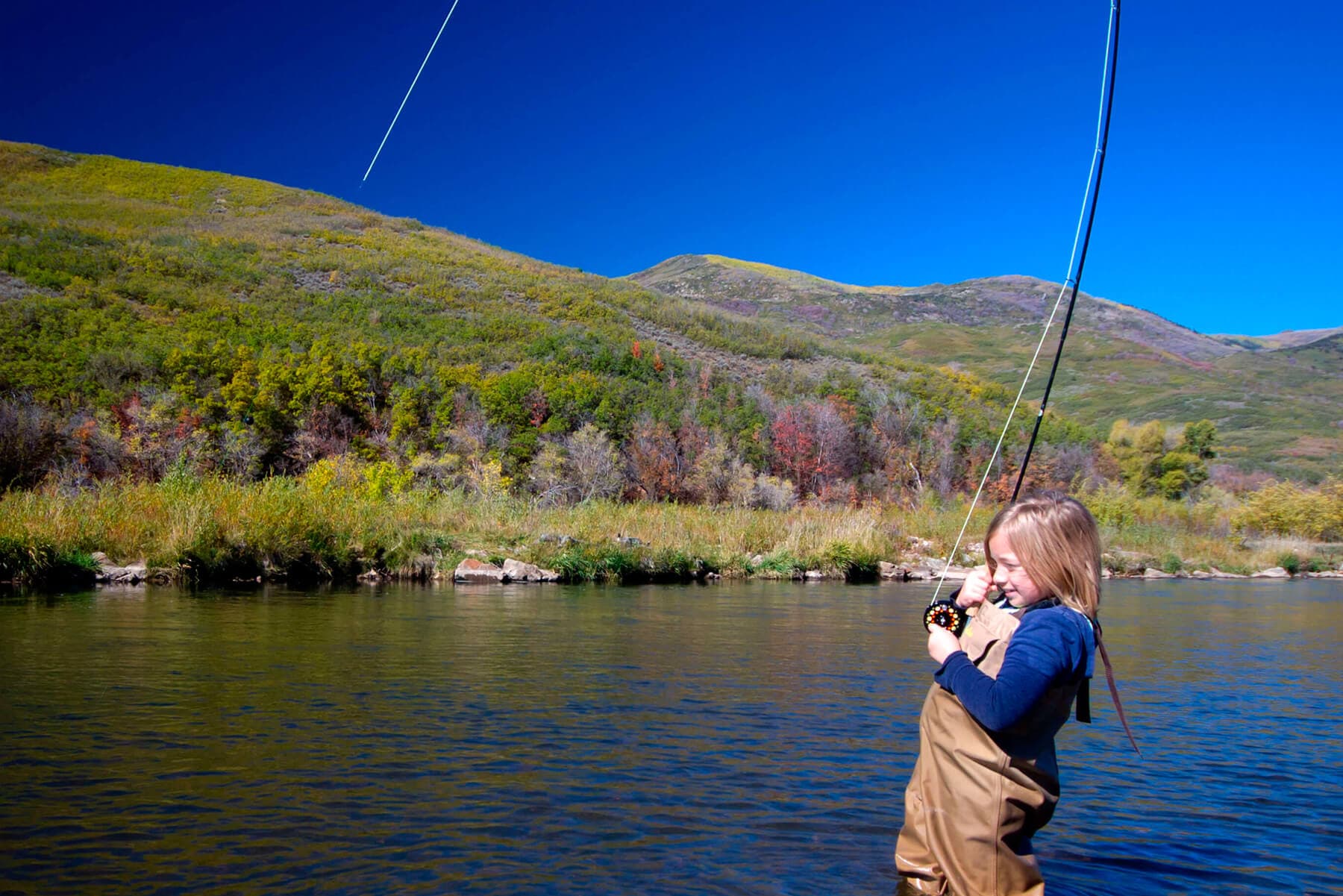 Angler fly fishing on a river beneath autumn Park City hills
