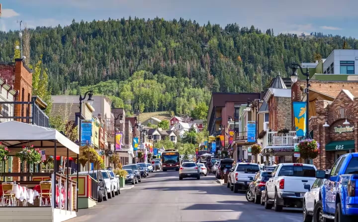 Park City's historic Main Street in summer, lined with shops and parked cars below a green hillside