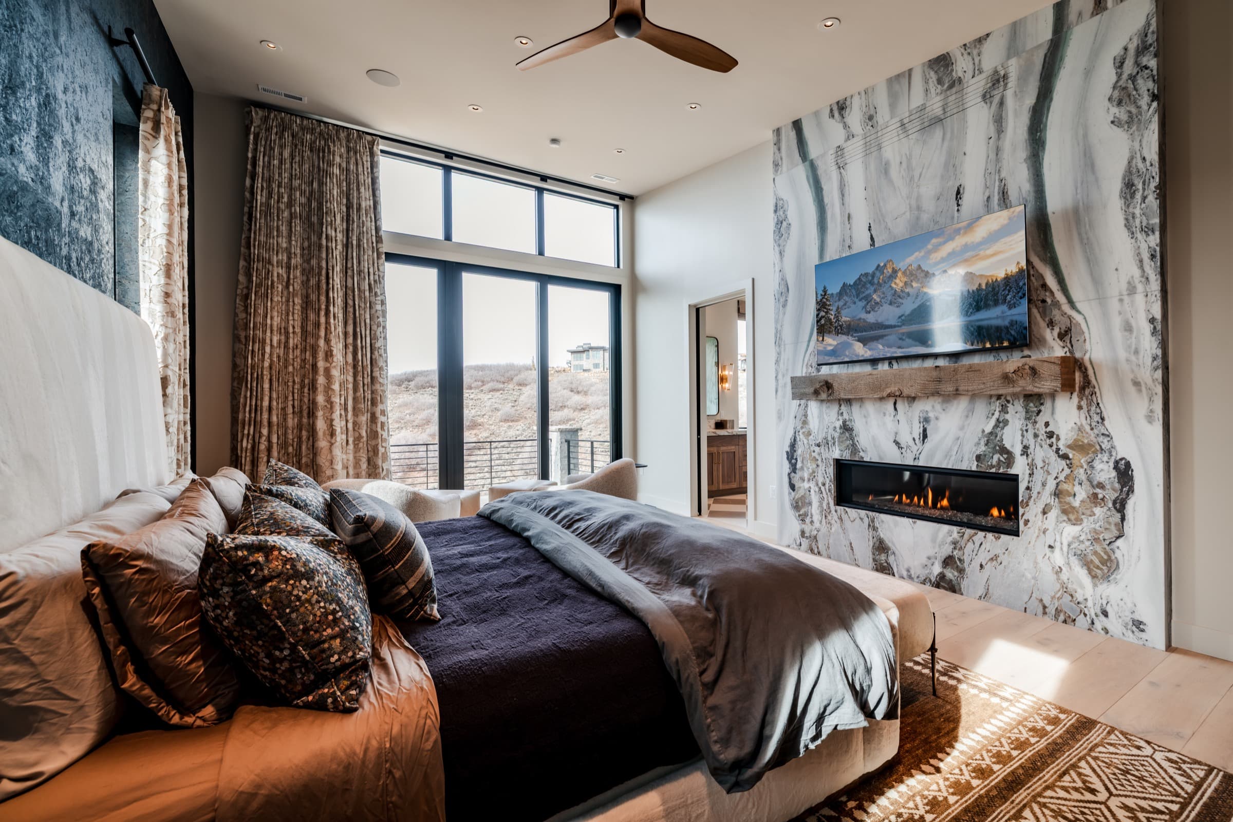 Park City master bedroom with marble fireplace, mountain view, and warm linens